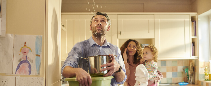 man holding buckets and pots cathcing water dripping from the ceiling with woman on the phone holding child looking at ceiling